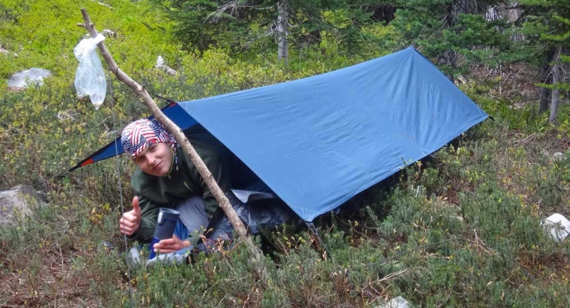a person gives a thumbs up while lying in a shelter they created on an outward bound trip